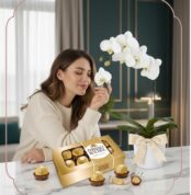 Mujer joven y elegante admirando una orquídea Phalaenopsis blanca con chocolates Ferrero Rocher en un ambiente de hogar lujos