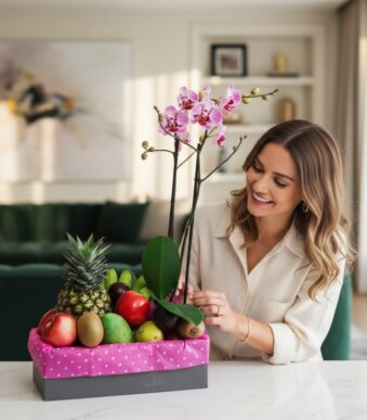Mujer sonriente admirando el Arreglo ANTONELLO con orquídea Phalaenopsis rosa y frutas frescas como piña, manzanas y kiwis, e