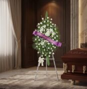 Pedestal conmemorativo Legado de Marcos con rosas blancas y lirios, cinta morada 'En Profunda Sinceridad', junto a un ataúd e