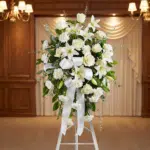 Pedestal conmemorativo Santuario para el Homenaje a PAREDES, con un elegante arreglo floral funerario de rosas blancas, lirio