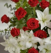 Primer plano macro de un arreglo fúnebre 'Pedestal Fúnebre Adoración' con rosas rojas vibrantes y lirios blancos puros, cubie