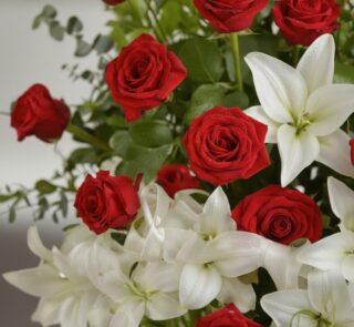 Primer plano macro de un arreglo fúnebre 'Pedestal Fúnebre Adoración' con rosas rojas vibrantes y lirios blancos puros, cubie