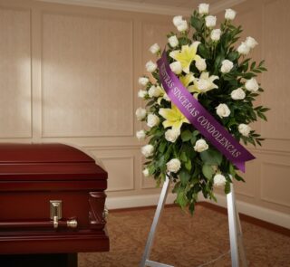Pedestal fúnebre "Luz de Jacinta" con rosas blancas y lirios amarillos, cinta morada con mensaje de condolencia, junto a un a