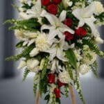 Fotografía macro premium del Pedestal Fúnebre Homenaje, mostrando lirios blancos, rosas rojas y follaje verde con rocío sutil