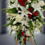 Fotografía macro premium del Pedestal Fúnebre Homenaje, mostrando lirios blancos, rosas rojas y follaje verde con rocío sutil