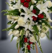 Fotografía macro premium del Pedestal Fúnebre Homenaje, mostrando lirios blancos, rosas rojas y follaje verde con rocío sutil