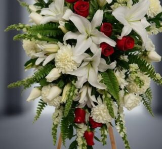 Fotografía macro premium del Pedestal Fúnebre Homenaje, mostrando lirios blancos, rosas rojas y follaje verde con rocío sutil
