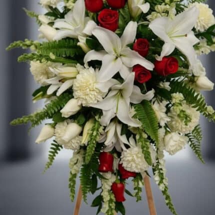 Fotografía macro premium del Pedestal Fúnebre Homenaje, mostrando lirios blancos, rosas rojas y follaje verde con rocío sutil