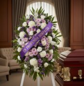 Pedestal fúnebre con flores blancas y moradas, cinta morada con mensaje 'En Profunda Simpatía', junto a un ataúd en sala de v