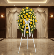 Pedestal fúnebre Legado Sereno con rosas y claveles amarillos, lazo blanco, en sala de velación elegante con cortinas y luz c