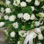 Fotografía macro premium del Pedestal Fúnebre Nunca te Olvidaré, mostrando rosas blancas, follaje verde con rocío sutil y una