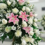 Fotografía macro premium del Pedestal Fúnebre Pasión, mostrando texturas hiperrealistas de pétalos blancos y lirios rosas con
