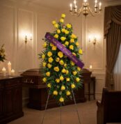 Pedestal fúnebre 'El Legado de Domingo' con rosas amarillas vibrantes y cinta morada 'En Sincera Condolencia' en sala de vela