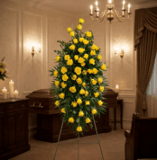 Pedestal fúnebre alto con rosas amarillas vibrantes y follaje verde, presentado en una elegante sala de velación con iluminac