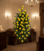 Pedestal fúnebre alto con rosas amarillas vibrantes y follaje verde, presentado en una elegante sala de velación con iluminac