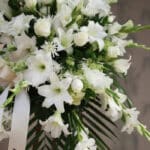 Fotografía macro premium de Pedestal Fúnebre Salvación, con lirios, rosas y gladiolos blancos, follaje verde y rocío sutil. C