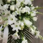 Fotografía macro premium de Pedestal Fúnebre Salvación, con lirios, rosas y gladiolos blancos, follaje verde y rocío sutil. C