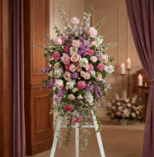 Pedestal funerario 'Luz de Elisa' con rosas, claveles y lirios en tonos pastel, realzado en una sala de velación con iluminac