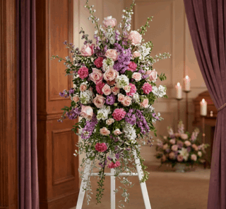 Pedestal funerario 'Luz de Elisa' con rosas, claveles y lirios en tonos pastel, realzado en una sala de velación con iluminac