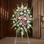 Pedestal floral funerario "El Legado de Josafat" con lirios rosas, rosas blancas y gladiolos en sala de velación elegante.
