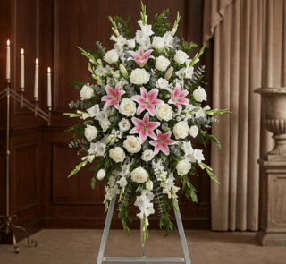 Pedestal floral funerario "El Legado de Josafat" con lirios rosas, rosas blancas y gladiolos en sala de velación elegante.