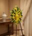 Pedestal de homenaje "El Legado de Sebastian" con un arreglo floral fúnebre de lirios y crisantemos amarillos, presentado ele