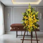 Pedestal de homenaje "El Legado de Sebastian" con un arreglo floral vertical de lirios, crisantemos y rosas amarillas, en una