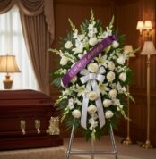 Imponente pedestal de honor Abdon con rosas blancas, lirios y gladiolos, adornado con una cinta morada que dice 'EN MEMORIA A