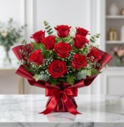 Ramillete o bouquet de rosas rojas frescas y abiertas con follaje verde, envuelto en papel rojo satinado con un lazo a juego,