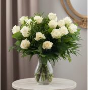 Ramo de 18 rosas blancas frescas en un jarrón de cristal, con follaje verde, sobre una mesa de mármol y fondo elegante.