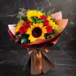Ramo Aurora de rosas rojas y girasoles vibrantes, envuelto elegantemente en papel de tonos tierra y atado con un lazo de saté