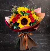 Ramo Aurora de rosas rojas y girasoles vibrantes, envuelto elegantemente en papel de tonos tierra y atado con un lazo de saté