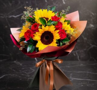 Ramo Aurora de rosas rojas y girasoles vibrantes, envuelto elegantemente en papel de tonos tierra y atado con un lazo de saté