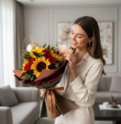 Mujer sonriente admirando el Ramo Aurora de Rosas y Girasoles, con girasoles vibrantes y rosas rojas, en un elegante salón de