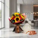 Ramo Aurora de rosas rojas y girasoles vibrantes, envuelto elegantemente, con tarjeta de regalo y cinta de satén sobre mármol