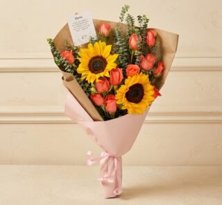 Ramo Beatrice con rosas salmón, girasoles vibrantes y eucalipto, envuelto en papel kraft y rosa, ideal para regalar en cualqu