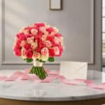 Ramo de 60 rosas fucsia y rosadas TRAVIATA sobre mesa de mármol con tarjeta de regalo y cinta rosa, listo para entregar.