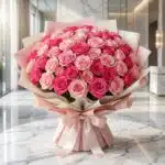 Impresionante ramo de 60 rosas fucsia y rosadas, con empaque coreano elegante, sobre mesa de mármol en floristería premium.
