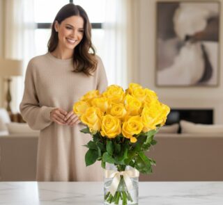 Mujer sonriente admirando un arreglo floral de 18 rosas amarillas en un jarrón de cristal con lazo, en un hogar de diseño luj