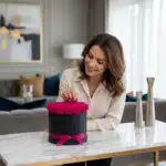Mujer elegante admirando y tocando delicadamente un arreglo floral de 21 rosas fucsia vibrantes en una caja negra con moño fu
