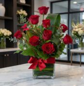 Arreglo floral Solitario ROSETTA con seis rosas rojas vibrantes en jarrón de cristal, lazo rojo, hojas verdes y mariposa deco
