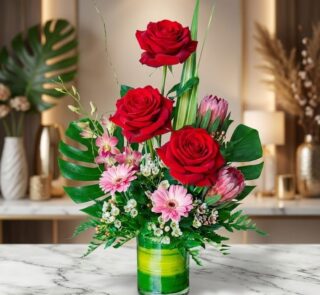 Arreglo floral exótico 'Solitario Pienso en Ti' con rosas rojas vibrantes, gerberas rosadas y follaje tropical en jarrón de c