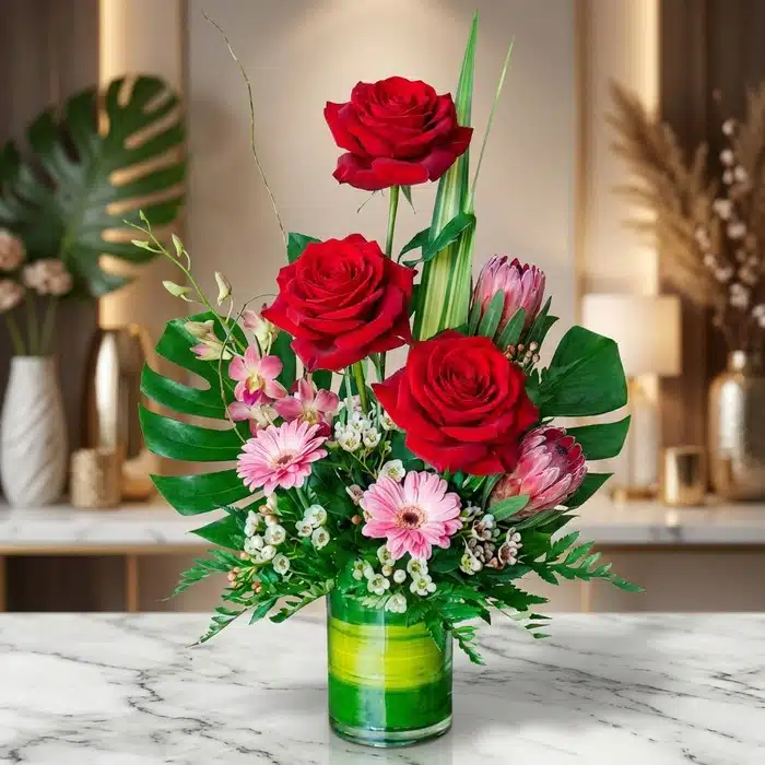 Solitario Pienso en Ti: Arreglo Floral Exótico de Rosas Rojas Arreglo floral exótico 'Solitario Pienso en Ti' con rosas rojas vibrantes, gerberas rosadas y follaje tropical en jarrón de c