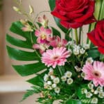 Primer plano extremo de un arreglo floral 'Solitario Pienso en Ti' con rosas rojas, gerberas rosas, orquídeas y follaje verde