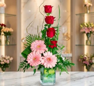 Arreglo floral exótico 'Solitario Tu Recuerdo' con tres rosas rojas en cascada, tres gerberas rosadas abiertas y follaje verd