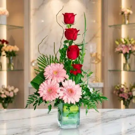 Arreglo floral exótico 'Solitario Tu Recuerdo' con tres rosas rojas en cascada, tres gerberas rosadas abiertas y follaje verd